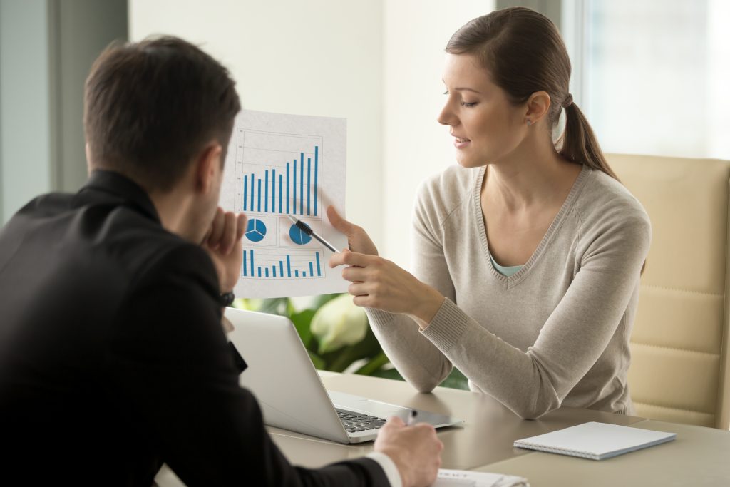 Mulher apresentando gráficos financeiros impressos para um homem em uma reunião de negócios.