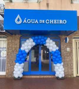 Fachada da loja Água de Cheiro com decoração de balões azuis e brancos em forma de arco na entrada.