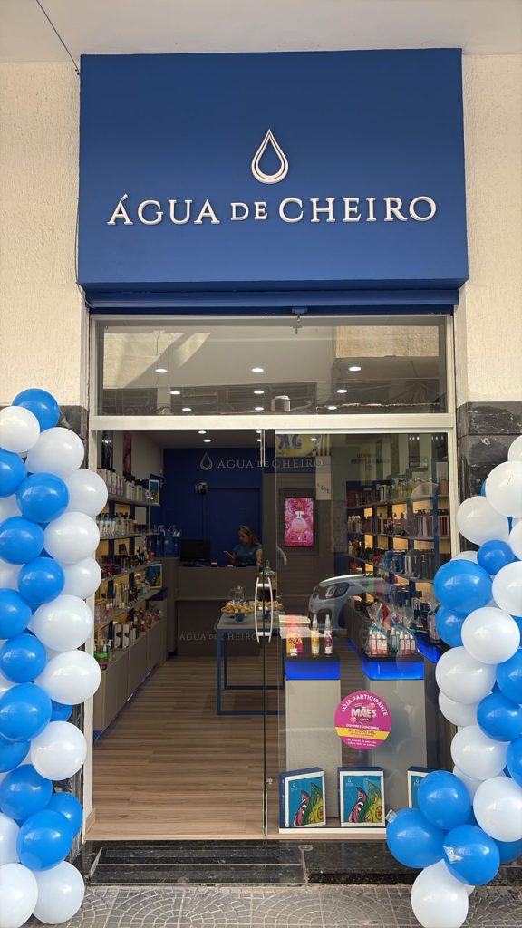 Fachada da loja Água de Cheiro com decoração de balões brancos e azuis, vitrine envidraçada e interior visível com produtos expostos.