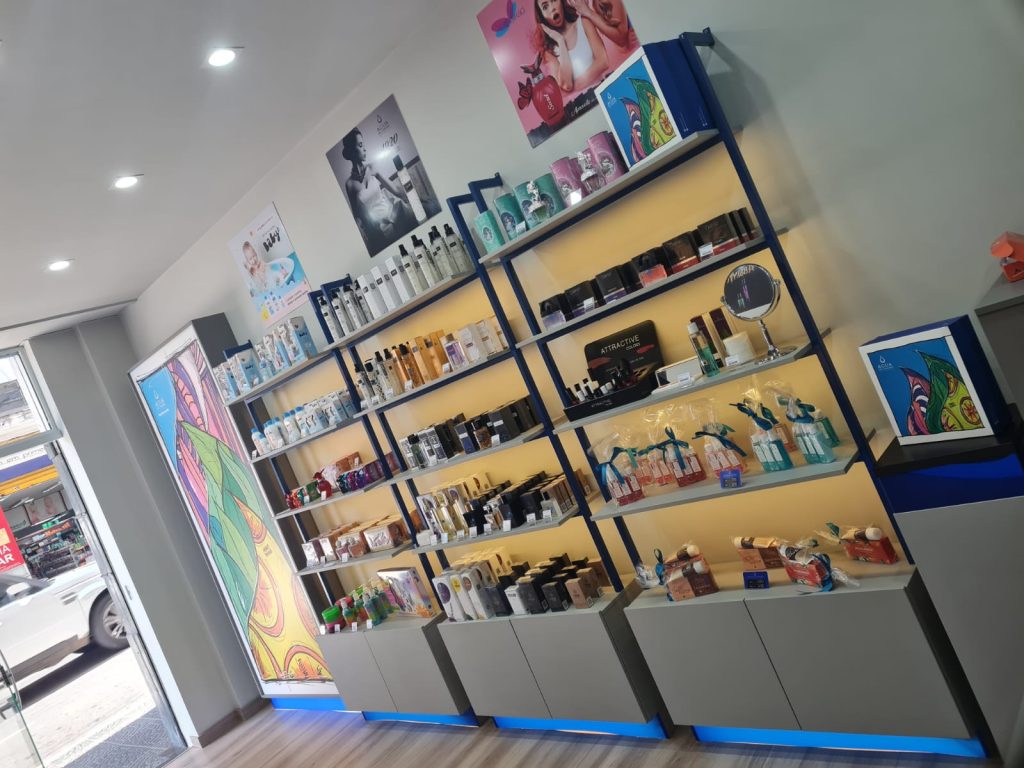 Interior da loja Água de Cheiro com prateleiras iluminadas, organizadas com produtos de perfumaria, cosméticos e kits presenteáveis.