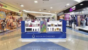 Quiosque da Água de Cheiro em shopping center, com perfumes e kits em exposição, cercado por outras lojas e com o McDonald's ao fundo.