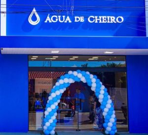 Fachada de uma loja da Água de Cheiro com letreiro branco sobre fundo azul e arco de balões azuis e brancos na entrada.