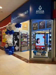 Fachada de loja Água de Cheiro decorada com balões azuis, brancos e prateados, com vitrine destacando campanha do Dia dos Namorados.
