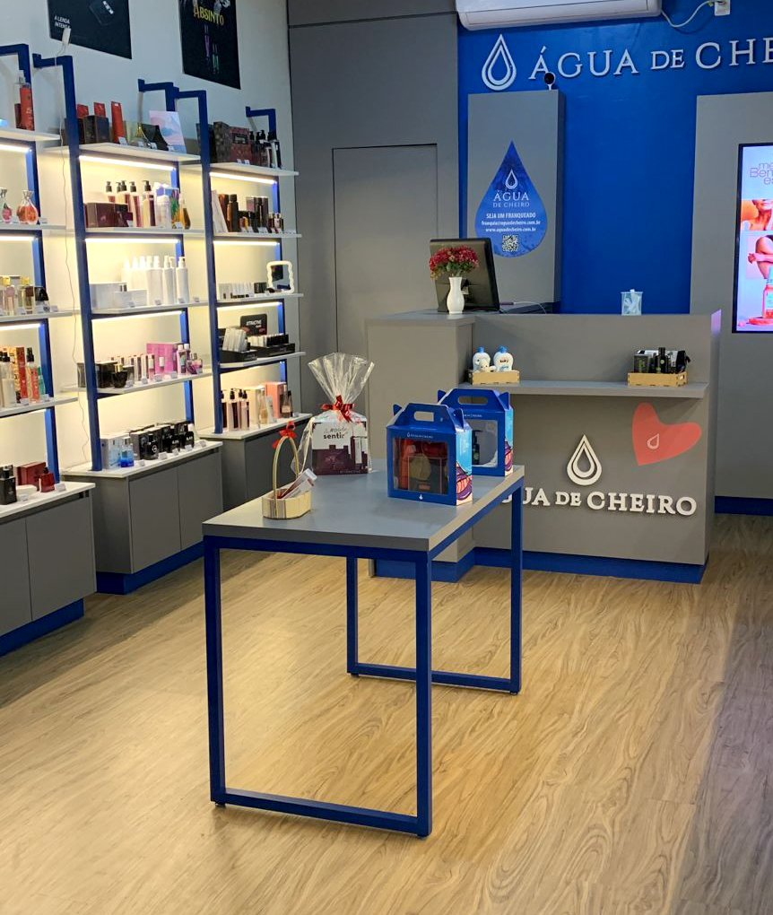 Interior de uma loja da Água de Cheiro com balcão de atendimento e prateleiras iluminadas exibindo perfumes e cosméticos.