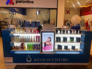 Quiosque da Água de Cheiro em shopping center, com prateleiras iluminadas exibindo perfumes, cremes e cosméticos organizados.
