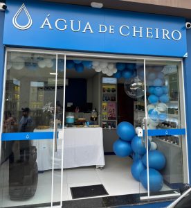 Fachada de uma loja Água de Cheiro decorada com balões azuis e brancos na entrada.