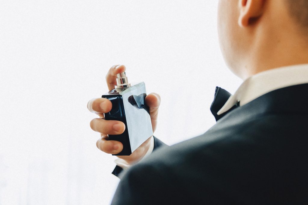 Homem aplicando perfume, vestido com smoking e gravata borboleta.